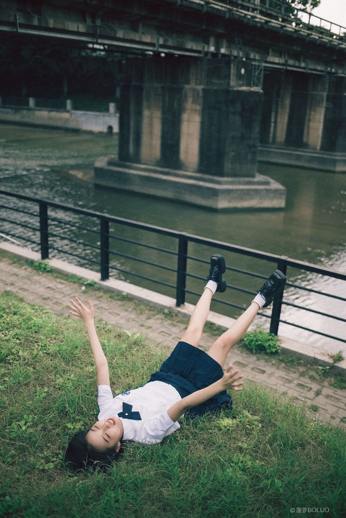 一位年轻女子躺在草地上 背景是带有桥的水域。