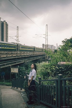 一个坐在围栏附近铁路轨道上的女人和一个站在桥上的人