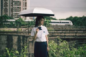 一位穿着黑色制服的年轻女子手持白色雨伞站在田野中