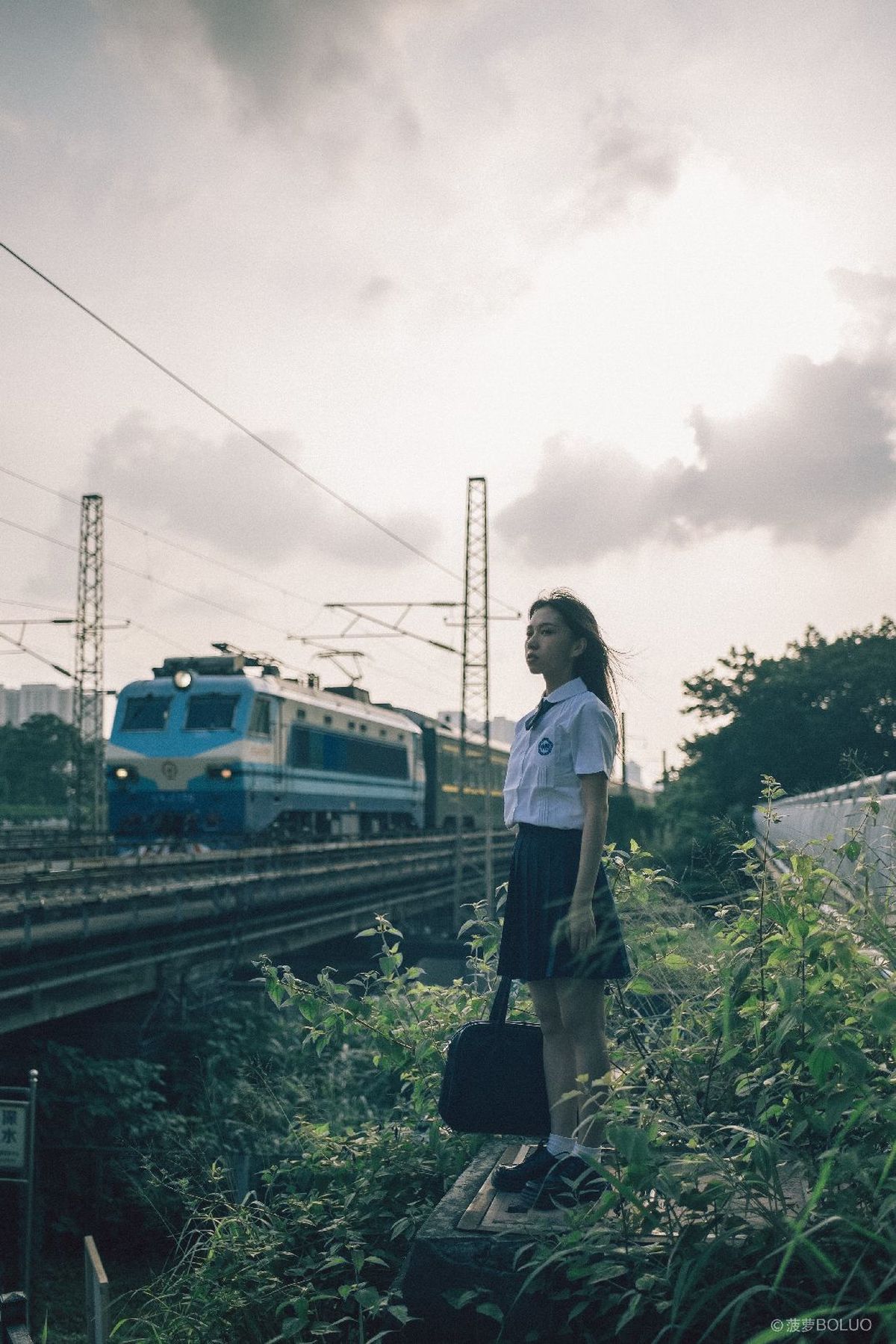 一位年轻女子带着行李站在火车轨道上 火车经过。