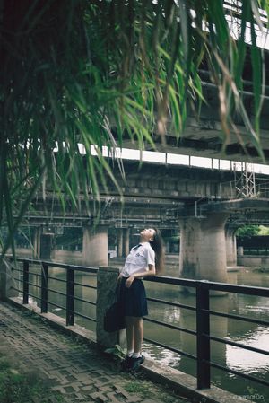 一位年轻女子站在伞下注视着桥下的水