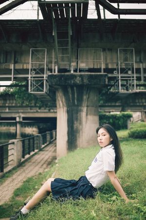 一位年轻女子坐在草地上 背景中有一座桥。