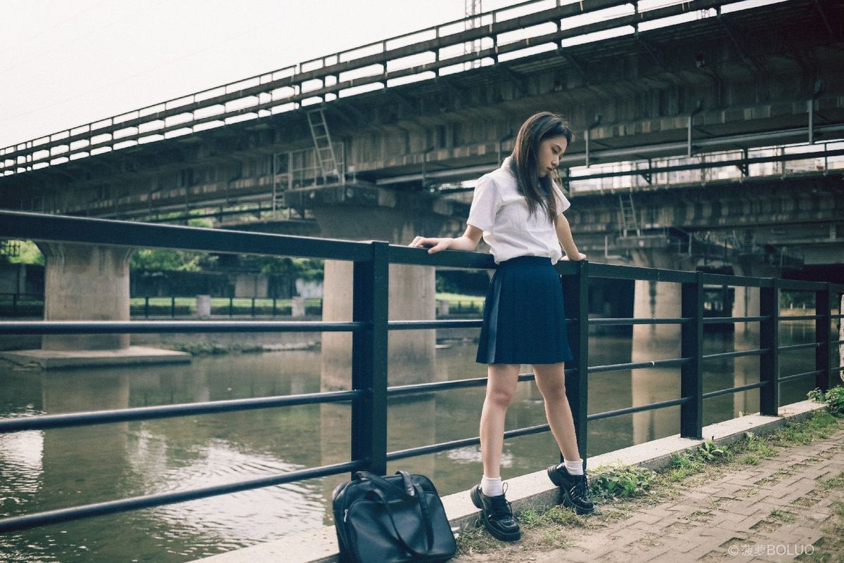 一位年轻女子站在一座河上的桥上 手提着旅行箱。
