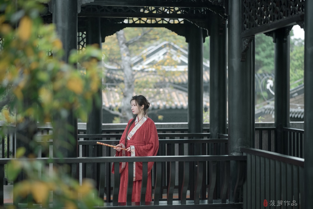 一位穿着日本红浴袍的女人走过一座日本寺庙的桥。
