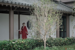 一位穿着红裙子的女人站在一栋建筑的庭院里 前方有一棵树。