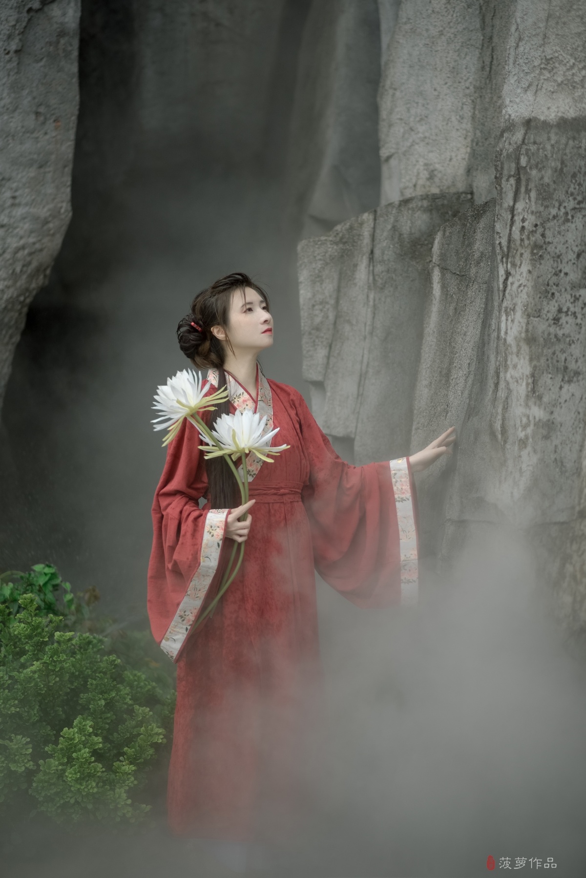 一位穿着传统红色和服的女孩手里拿着白色的花站在瀑布前