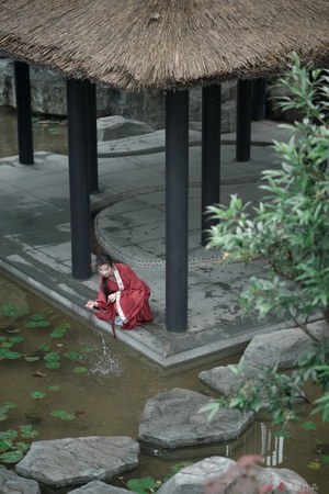 一位穿着红衣服的女士坐在一个小池塘的水中央