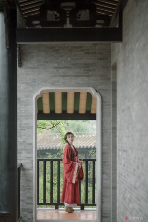 一个穿着传统红色长袍的年轻女孩站在一栋建筑物的门口。