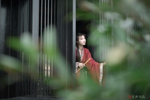 一位穿着红裙子的年轻女子站在一栋建筑物的窗户前