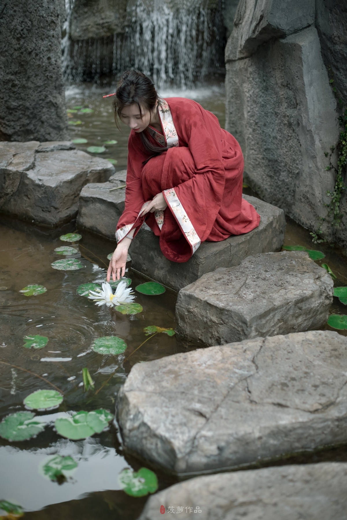一个穿着红袍的年轻女孩蹲在岩石上 从池塘里喝水。