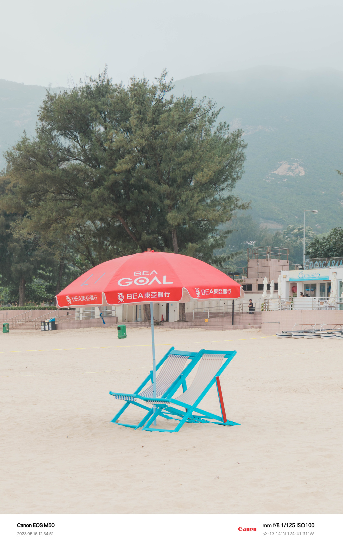 坐在沙滩上的一个蓝色沙滩椅在红色雨伞下