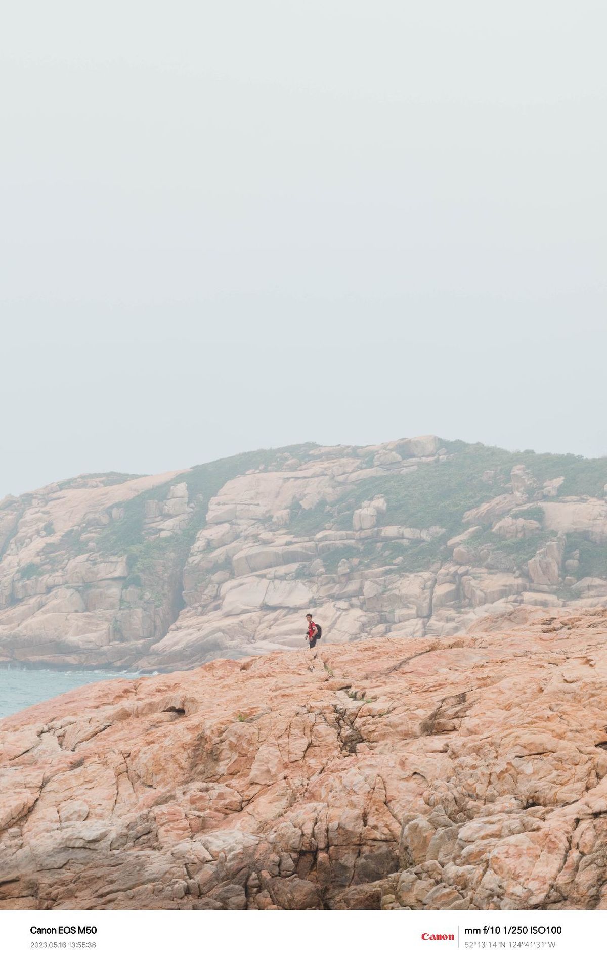 一个站在岩石悬崖上 眺望海洋 远处有岩石和山的人。