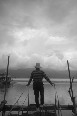 站在湖边码头上的一名戴帽子的男子