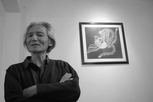 一张黑白照片 一位男子双臂交叉站在一幅女性画像和一幅画的前面。
