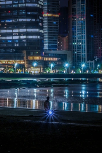 夜晚坐在水边 城市在背景中熠熠生辉的男子