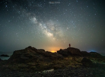 夜晚在岩石上站在海边的男人 天空中繁星闪烁。