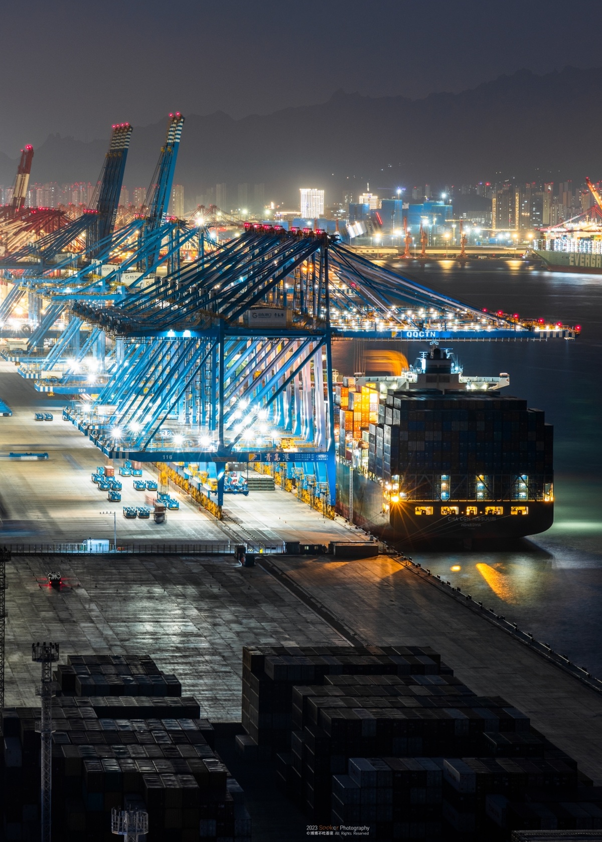 停泊在港口的一艘大型货轮在夜晚被大型起重机照亮 