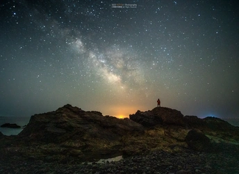 夜晚在星空下 站在岩石旁的海边的一个男人