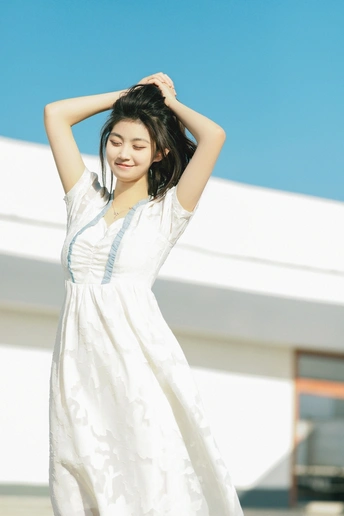 身穿白色连衣裙的年轻美女在蓝天下摆姿势