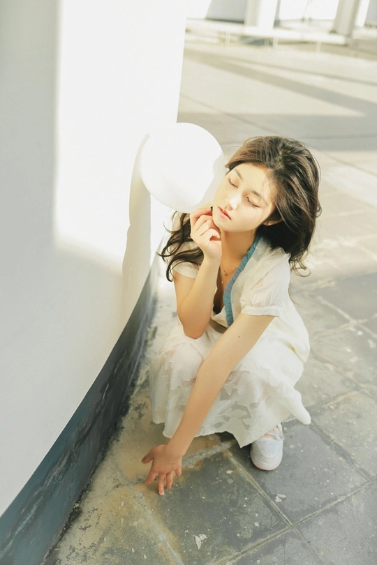 一个穿着白色连衣裙的漂亮年轻女子坐在地板上 从窗户向外看