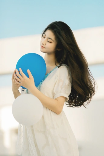 一个穿着白色连衣裙 手里拿着一个蓝色球的漂亮年轻女子