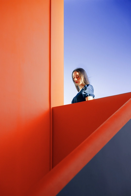 一位女士站在一组橙色楼梯上 对着蔚蓝的天空。