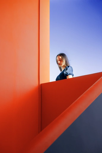 一位女士站在一组橙色楼梯上 对着蔚蓝的天空。