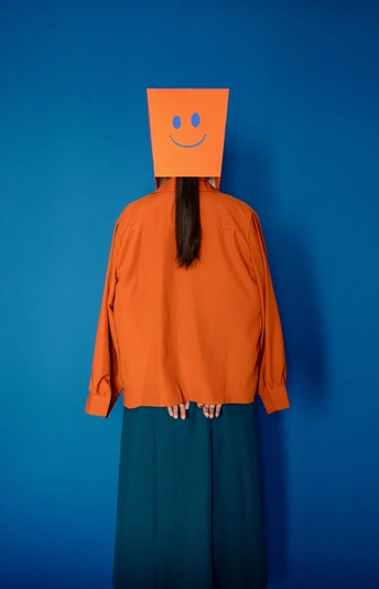 一个人头戴橙色衬衫 衬衫上有橙色笑脸图案 站在蓝色背景前