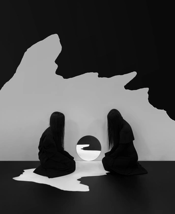 黑白色调的艺术作品 描绘了一位 woman 和一位 girl 坐在洞穴前的一盏灯下。