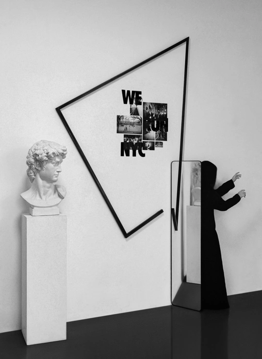 一张黑白照片 一个人站在一个头像雕塑和一个挂钟的墙边。