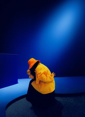 一位穿着黄色和橙色衣服的女人坐在蓝色舞台前。