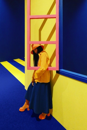一位站在黄色墙壁的房间里 有粉色梯子靠在蓝色墙壁上的女性。
