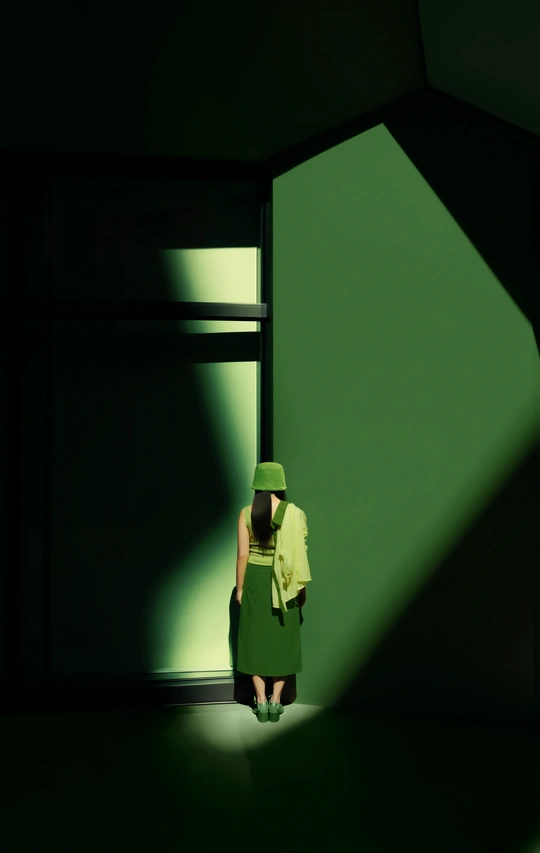 一个穿着绿色外套和帽子站在光线昏暗的房间里的小女孩