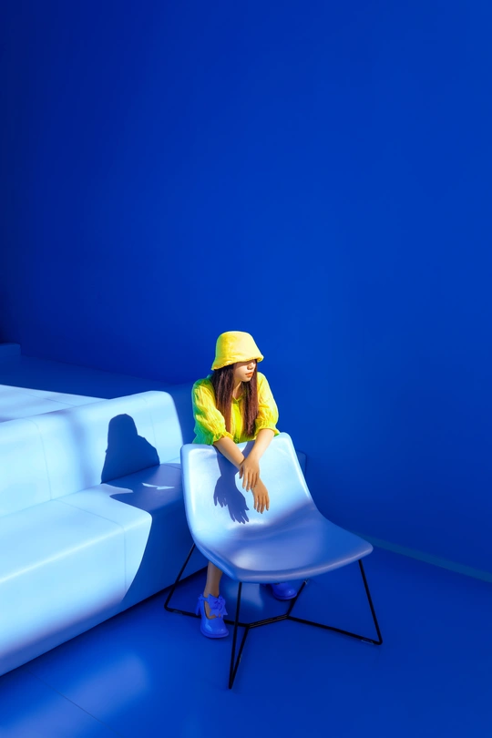 一个小女孩戴着黄帽子坐在一个白色的椅子上 在一个蓝色的房间里。