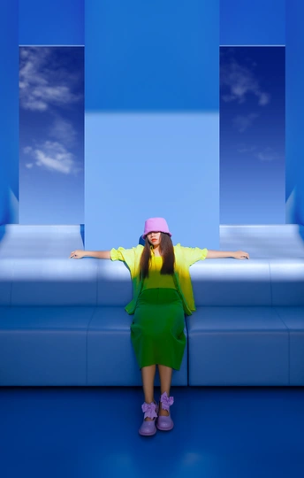 一个小女孩穿着绿色连衣裙和粉色帽子坐在蓝色沙发上的一间房间里