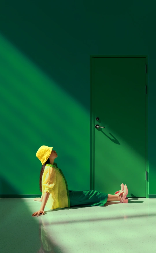 一个穿着黄色雨衣的年轻女子坐在一个绿色墙壁和绿色门的房间里