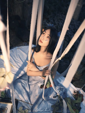 一个穿着蓝色连衣裙的年轻女子坐在一个白色秋千上