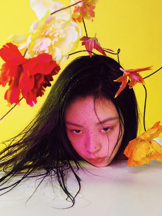 一位头戴鲜花的年轻女子 背景为黄色。