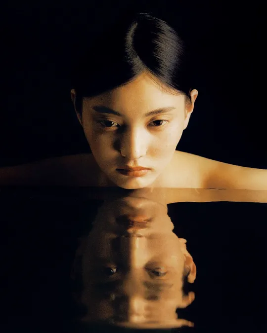 一位女子用手捂住脸 她的手臂浸在水中 形成一幅肖像。