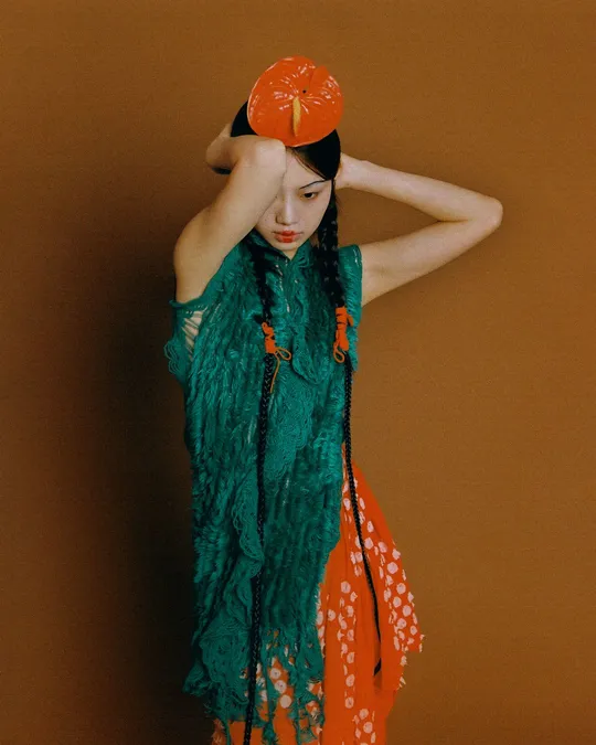 一位戴橙色帽子、绿色连衣裙的女士举着一把红色雨伞在头上。