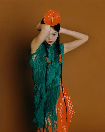 一位戴橙色帽子、绿色连衣裙的女士举着一把红色雨伞在头上。