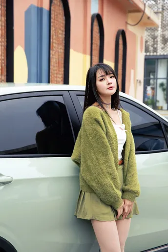 一位穿着绿色外套的年轻女子靠在一辆汽车上