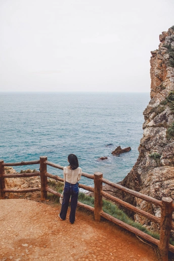 一位站在围栏边缘 凝视着悬崖 overlooking 水域的海洋 海岸线上的女性。