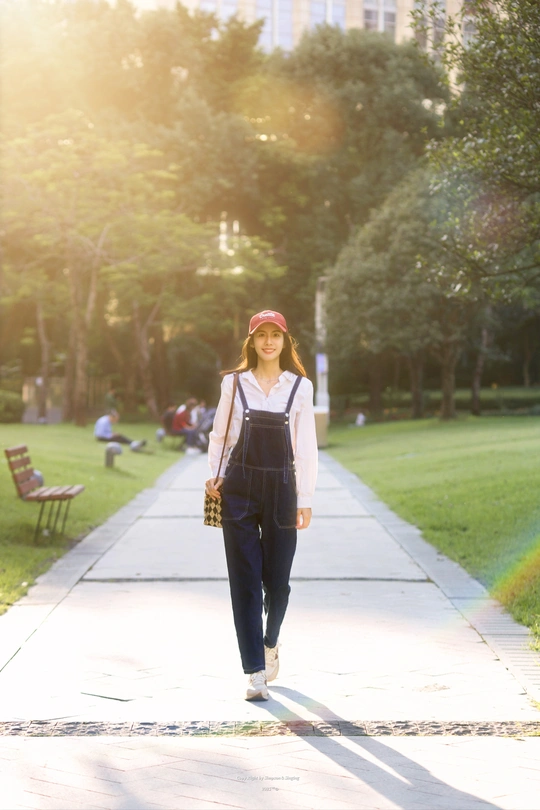 一位穿着工作服和戴着帽子的年轻女子正在公园的小径上走。