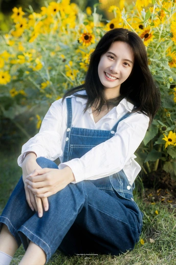 一位穿着工作服的年轻女子坐在草地前 面前是一片黄色的花田。