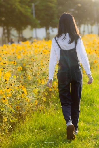 一位穿着工作服的年轻女子穿过一片黄花的田野。