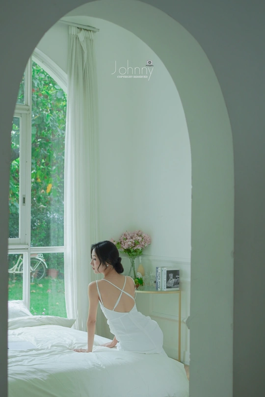 一个穿着白色连衣裙的女人坐在卧室的床上