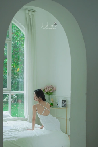 一个穿着白色连衣裙的女人坐在卧室的床上