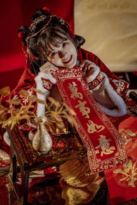 一个穿着传统服装的年轻女孩坐在桌子旁 手里拿着一个洋娃娃。