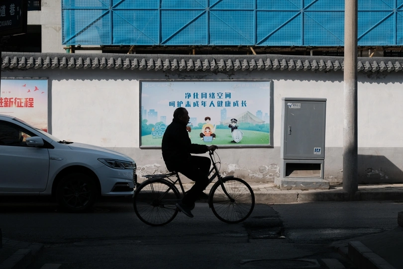 一个男人骑自行车穿过一个有女性广告牌的建筑物前面的街道。